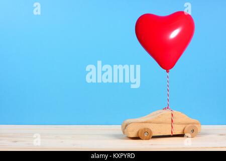 Giocattolo di legno auto con un cuore rosso palloncino contro uno sfondo blu. Il giorno di San Valentino o il concetto di amore. Foto Stock