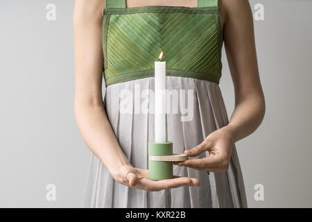 Deliziosa ragazza può contenere un metallo-legno candelabro verde con una candela che brucia nelle sue mani sullo sfondo luminoso in studio. Indossa un colorato Foto Stock