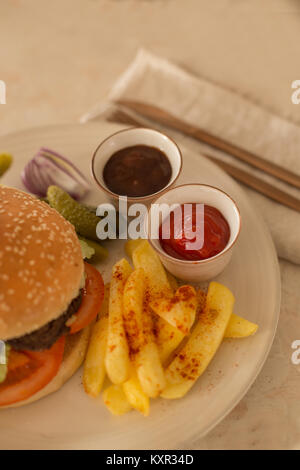 Pomodoro e salsa barbecue in piccole ciotole di ceramica con le patatine e hamburger servito su una piastra di ceramica Foto Stock