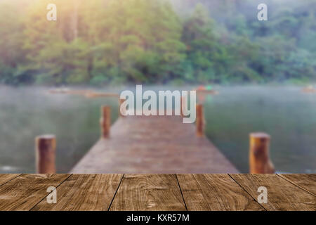 Tavolo in legno con blur ponte in legno sul lago dock in background di foresta Foto Stock