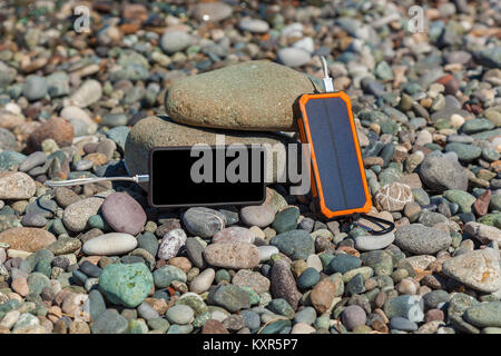 Il poverbank giace sulla ghiaia dal mare e carica il telefono. Powerbank carica il telefono. Foto Stock