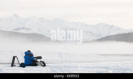 Silhouette di fotografo sulla neve con treppiede e fotocamera . Inverno mattina nebbia. Foto Stock