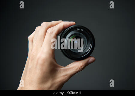 Mano d'uomo in possesso di un obiettivo della telecamera su uno sfondo nero Foto Stock