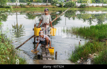 Gli uomini la raccolta di acqua di stagno in Yangon, Myanmar Foto Stock