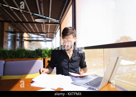 Lavoratore di ufficio ordinamento di carte sul tavolo vicino al computer portatile. Foto Stock