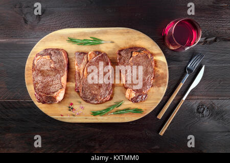 Una foto aerea di tre fette di carne cotta, filetti di manzo, ripresa dall'alto sul buio rustica con rametti di rosmarino, sale, pepe, vino, Foto Stock