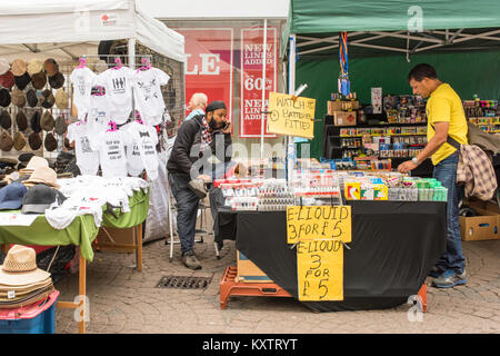 Giorno di mercato a Ramsgate centro città. Un commerciante asiatico che vende diversi articoli sul suo stallo. Foto Stock