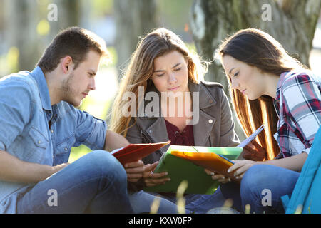 Un gruppo di tre studenti di note di lettura seduta sul prato di un parco Foto Stock