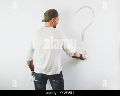 Guy la cancellazione di un punto interrogativo su un muro bianco utilizzando un rullo Foto Stock