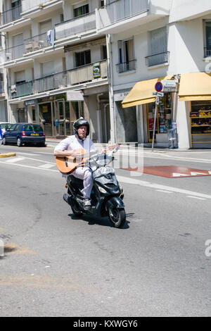 Uomo che cavalca scooter giù per la collina e di suonare una chitarra a Nizza Francia Foto Stock