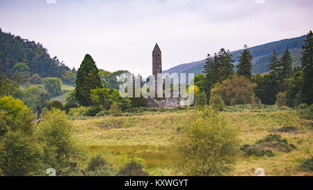 Scenic Glendalough Valley con la torre rotonda e rovine medievali di insediamento monastico fondato nel VI secolo da San Kevin Foto Stock