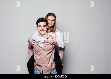 Felice uomo informale dando bella ragazza piggy back su sfondo grigio Foto Stock