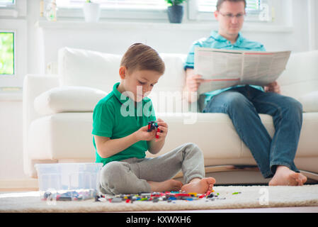 Little Boy gioca con kit di costruzione, padre leggere giornali Foto Stock