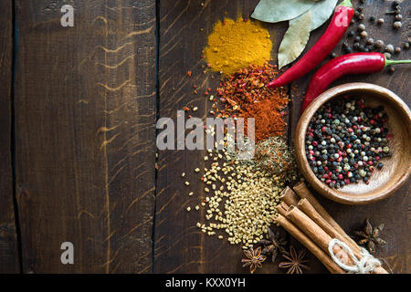 Pepe in ciotola con sparsi di erbe e di spezie, foglie di alloro, il peperoncino sul piano portapaziente in legno Foto Stock