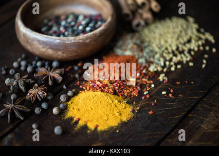 Diversi tipi di pepe in un recipiente e spezie con erbe sparsi sul tavolo in legno Foto Stock