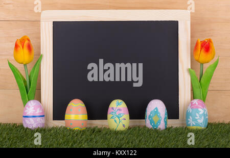 Colorate le uova di Pasqua e tulipani con un gesso bianco bordo per spazio di copia Foto Stock