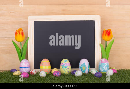 Colorate le uova di Pasqua, candy e tulipani con un gesso bianco bordo per spazio di copia Foto Stock