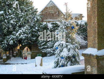 Albero di natale con baubles blu in St Edwards sagrato nella neve. Stow on the Wold, Cotswolds, Gloucestershire, Inghilterra Foto Stock