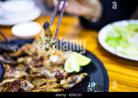Bacchette tenendo grigliata di pesce Salmone testa da una piastra, spuntino cinese Foto Stock