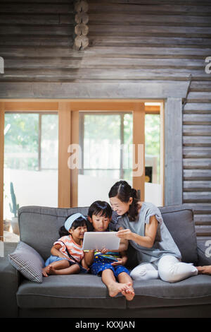 Donna, ragazzo e ragazza seduta su un divano grigio, guardando a tavoletta digitale. Foto Stock