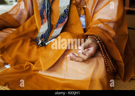 Chiusura del monaco buddista che indossa golden robe seduta zampe trasversale sul pavimento, meditando, buddista gesto a mano. Foto Stock