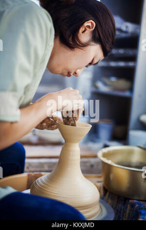 Donna che lavorano in una porcellana giapponese workshop, seduti su un tornio del vasaio, gettando la ciotola. Foto Stock