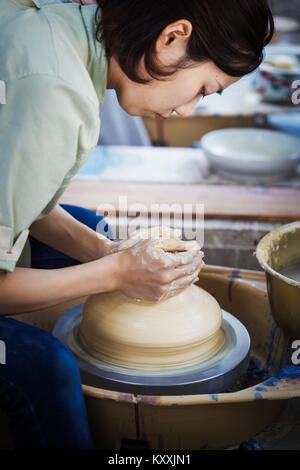 Donna che lavorano in una porcellana giapponese workshop, seduti su un tornio del vasaio, gettando la ciotola. Foto Stock