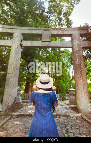 Vista posteriore del giovane donna indossa vestito blu e cappello in piedi presso lo Shintoismo Sakurai Santuario, Fukuoka, Giappone. Foto Stock