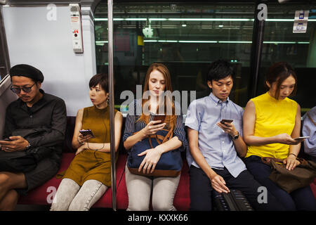 Cinque persone sedute sidy dal lato su un treno della metropolitana di Tokyo pendolari. Foto Stock