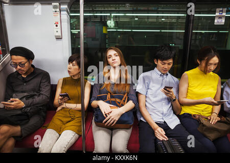 Cinque persone sedute sidy dal lato su un treno della metropolitana di Tokyo pendolari. Foto Stock