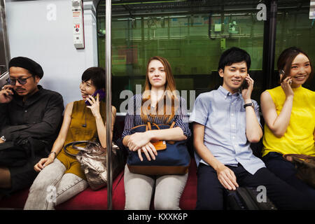 Cinque persone sedute sidy dal lato su un treno della metropolitana di Tokyo pendolari. Foto Stock