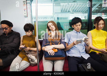 Cinque persone sedute sidy dal lato su un treno della metropolitana di Tokyo pendolari. Foto Stock