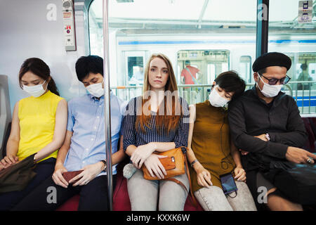 Cinque persone che indossano maschere antipolvere sidy seduta a fianco su un treno della metropolitana di Tokyo pendolari. Foto Stock