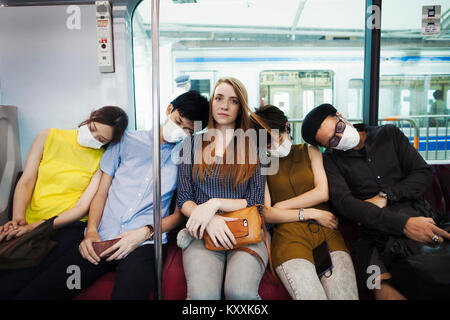 Cinque persone che indossano maschere antipolvere sidy seduta a fianco su un treno della metropolitana di Tokyo pendolari. Foto Stock