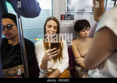 Tre persone sedute sidy dal lato su un treno della metropolitana di Tokyo pendolari. Foto Stock