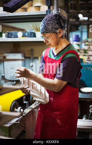 Donna che lavorano in una porcellana giapponese workshop, indossando il grembiule, la holding di colore bianco porcellana oggetto. Foto Stock