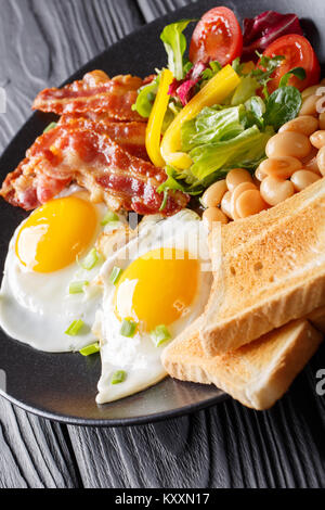 Ricca prima colazione: uova fritte con pancetta, fagioli, toast e fresca insalata di verdure su una piastra sul piano verticale.