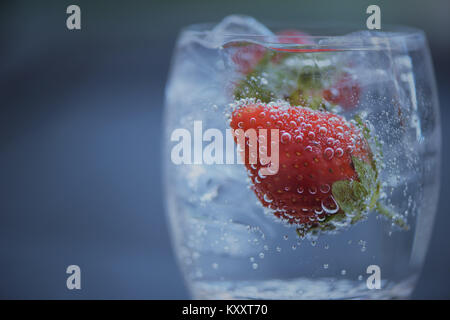 Rinfrescare cibi e bevande macro close up immagine fotografia di frutta rossa fragola in un bicchiere di cubetti di ghiaccio e frizzante acqua naturale con uno spazio Foto Stock