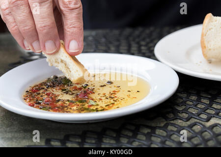 Persona pane immersione in un esperto di olio di oliva su una piastra bianca Foto Stock