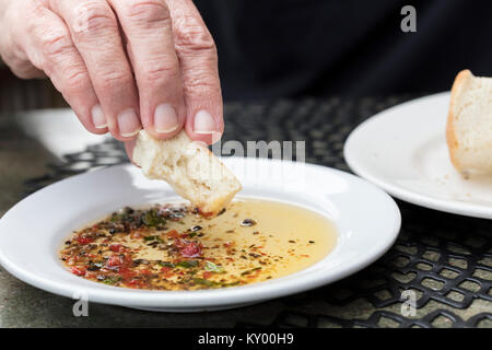 Persona pane immersione in un esperto di olio di oliva su una piastra bianca Foto Stock