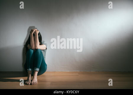 Depressione femmina giovane adolescente di aver abusato di problema sensazione di sofferenza e di seduta sul pavimento di legno utilizzando mani nascondendo al grido di sfondo bianco. Foto Stock