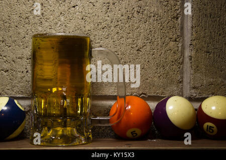 Il freddo boccale di birra in un prossimo a più colorate palle da biliardo su un sfondo di calcestruzzo Foto Stock