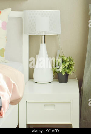 Lampada bianca e fiori in vaso sul comodino accanto al letto Foto Stock