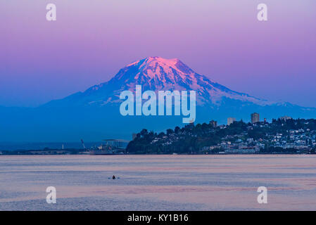 Mt Rainier sembra passare il puntatore del mouse sopra il centro cittadino di Tacoma come il sole di setting trasforma il cielo e la montagna sfumature di rosa e viola Foto Stock