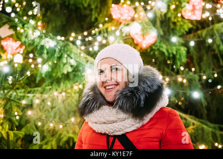 Tallinn, Estonia. Giovane bella bella ragazza caucasica Donna vestita in rosso giacca e cappello bianco per godersi la vita e sorridente su sfondo Natale Tr Foto Stock