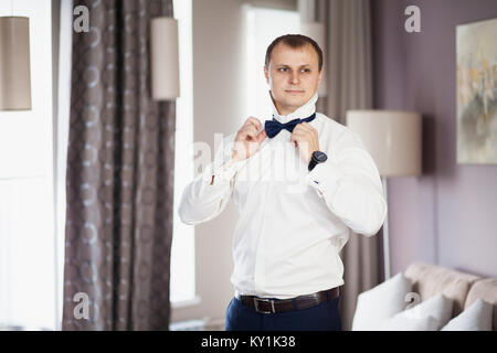 L uomo lo sposo in camicia bianca mettendo sul tirante butterfly Foto Stock