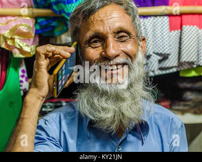 Ritratto di un anziano, barbuto uomo musulmano tramite telefono cellulare, felice e sorridente. Foto Stock