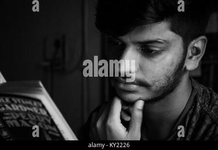In bianco e nero di close-up ritratto di una giovane adulto ragazzo indiano la lettura di un libro con la mano sul mento, pensando gesto. Foto Stock