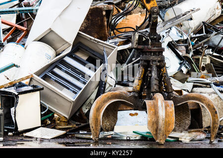 Potente meccanico afferra il braccio è la forza che muove il vecchio rottame metallico e utilizzati apparecchi elettrodomestici in un cantiere di scarto. Foto Stock