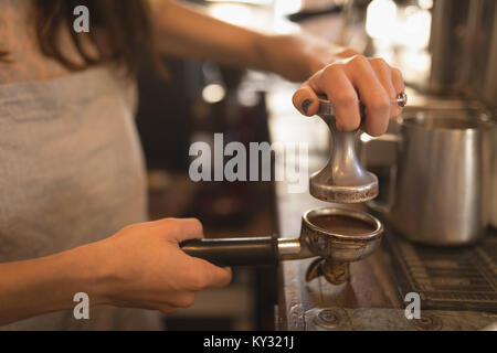 Barista utilizzando un dispositivo antimanomissione per premere il caffè macinato in un portafilter Foto Stock